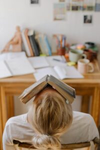 勉強途中でつかれて本を顔に載せてのけぞる女性。